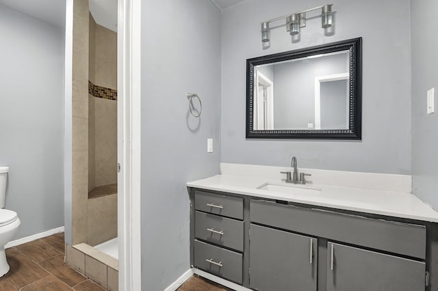 bathroom with wood-type flooring, vanity, a tile shower, and toilet