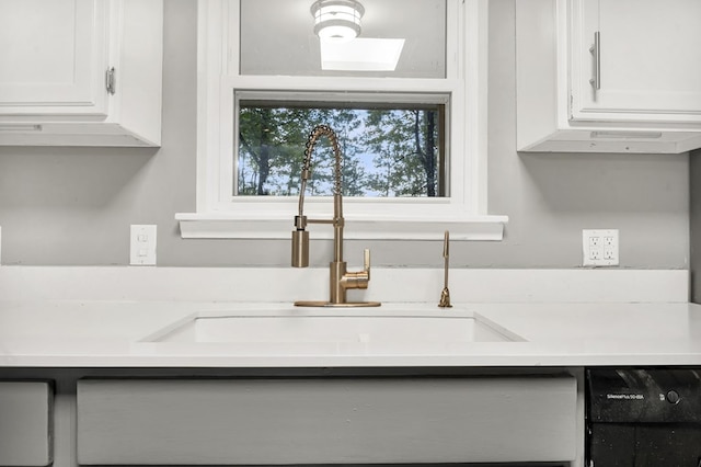 kitchen with dishwasher, white cabinetry, and sink