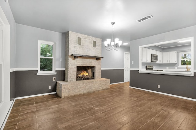 unfurnished living room with a chandelier, dark hardwood / wood-style floors, and a brick fireplace