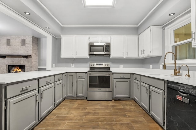 kitchen with gray cabinetry, sink, stainless steel appliances, a stone fireplace, and kitchen peninsula