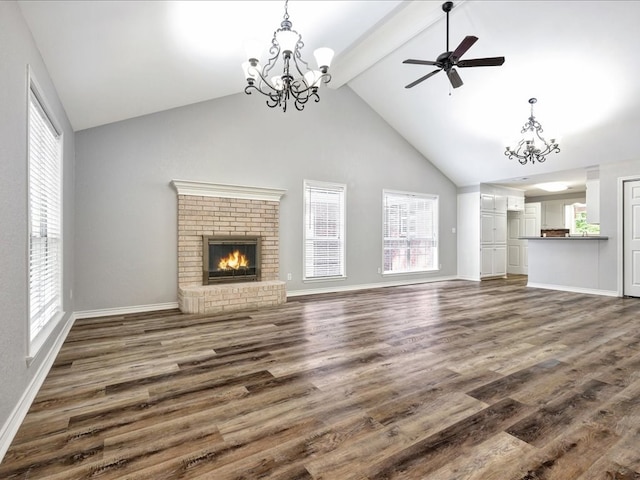 unfurnished living room with dark wood-type flooring, a brick fireplace, ceiling fan with notable chandelier, and beamed ceiling