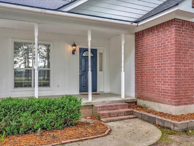 doorway to property featuring brick siding, roof with shingles, and covered porch