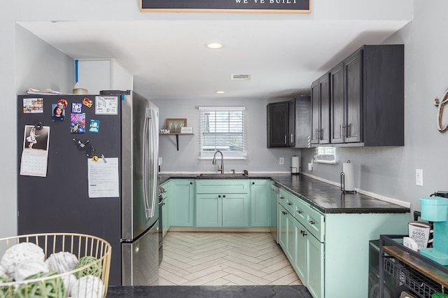 kitchen featuring sink, green cabinets, light parquet flooring, and appliances with stainless steel finishes