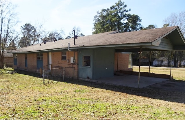 rear view of property with a carport, a patio area, fence, and a lawn