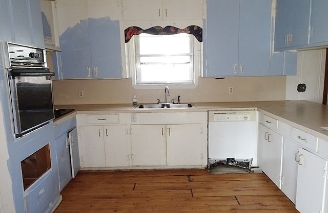 kitchen with white dishwasher, wood finished floors, a sink, white cabinetry, and black oven