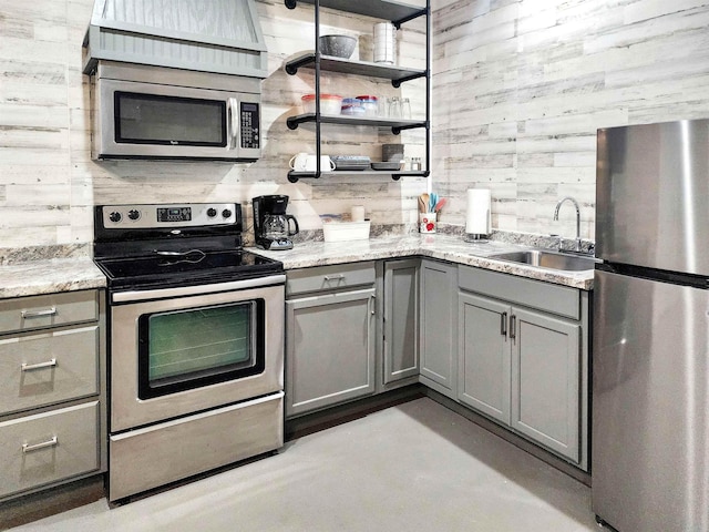 kitchen with gray cabinets, a sink, stainless steel appliances, wood walls, and decorative backsplash