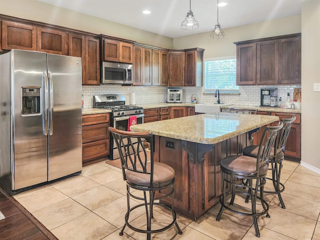 kitchen with a kitchen island, a sink, stainless steel appliances, a kitchen breakfast bar, and backsplash