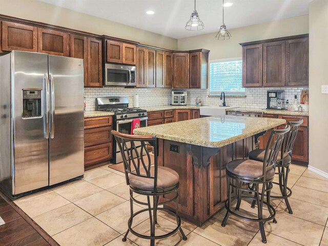 kitchen featuring a breakfast bar, appliances with stainless steel finishes, light stone countertops, a kitchen island, and decorative light fixtures