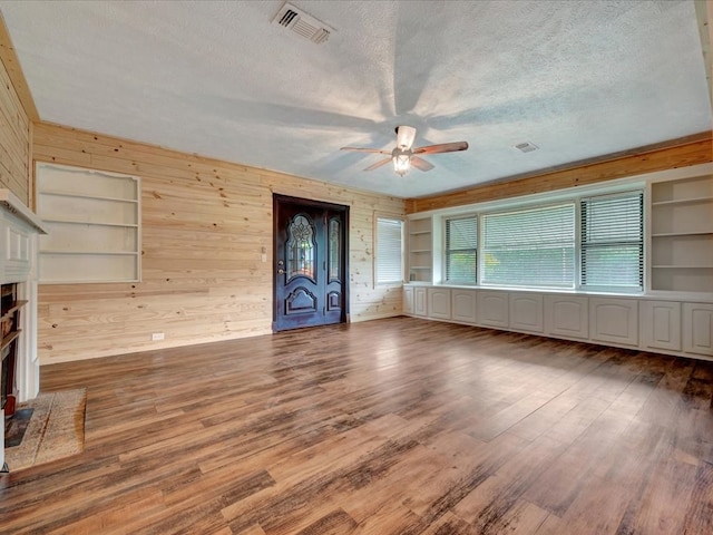 2524 US Highway 69 N, Lufkin, TX 75904 - unfurnished living room with ceiling fan, wood walls, a textured ceiling, a fireplace with flush hearth, and wood finished floors