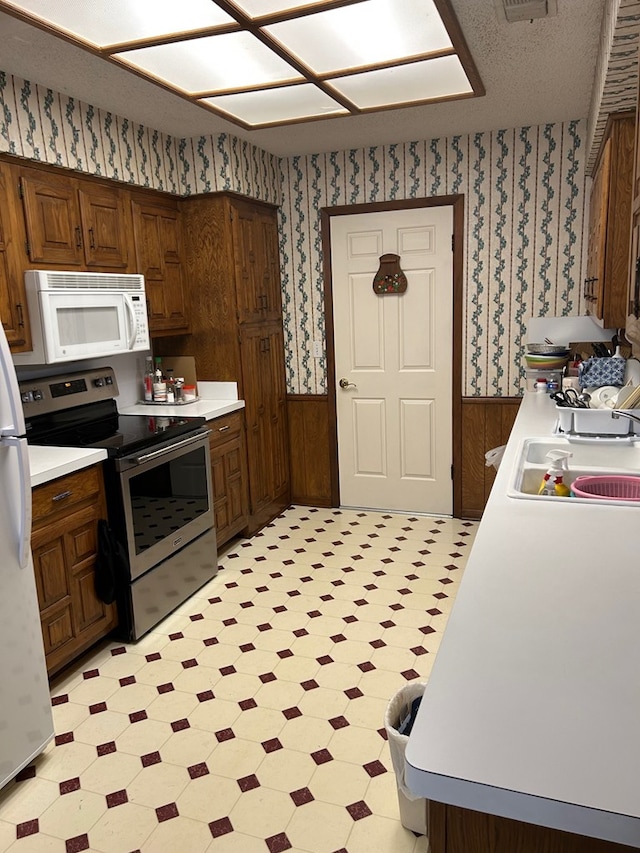 kitchen featuring white appliances, a textured ceiling, and wood walls