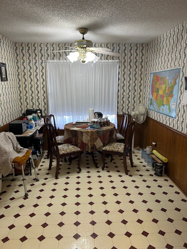 dining room featuring ceiling fan, a textured ceiling, and wood walls