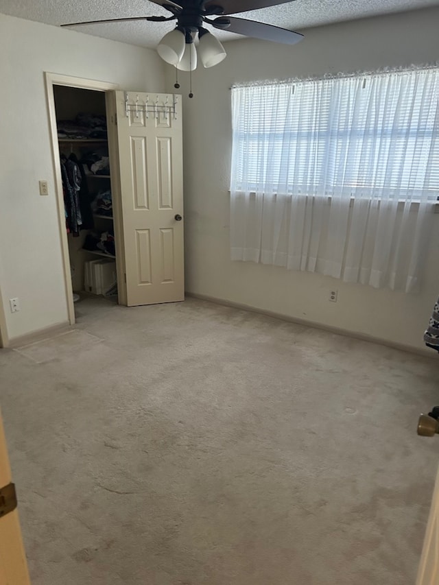 unfurnished bedroom with ceiling fan, light colored carpet, and a textured ceiling