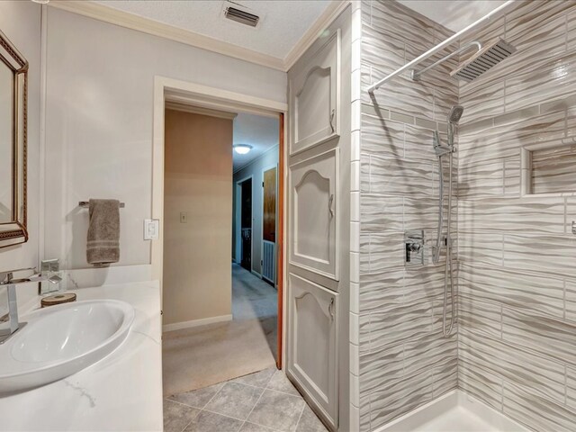 bathroom with vanity, tile patterned floors, crown molding, tiled shower, and a textured ceiling