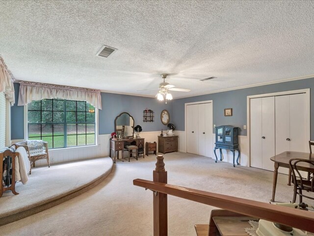 interior space with a textured ceiling, ceiling fan, two closets, and ornamental molding