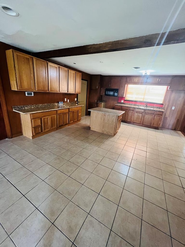 kitchen with beam ceiling, wood walls, a kitchen island, and light tile patterned floors