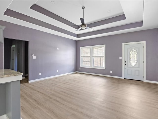 unfurnished living room with ceiling fan, a raised ceiling, and light wood-type flooring