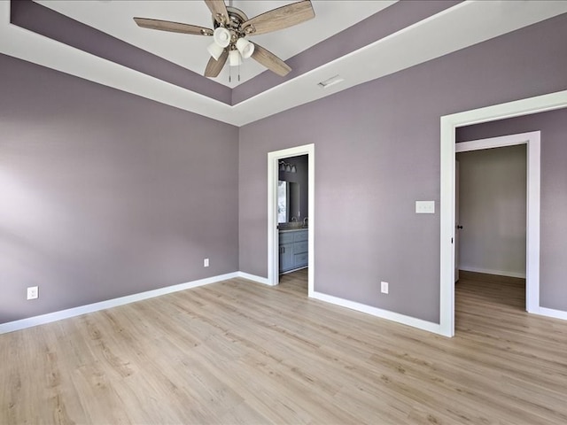 unfurnished bedroom featuring connected bathroom, ceiling fan, a tray ceiling, a closet, and light wood-type flooring