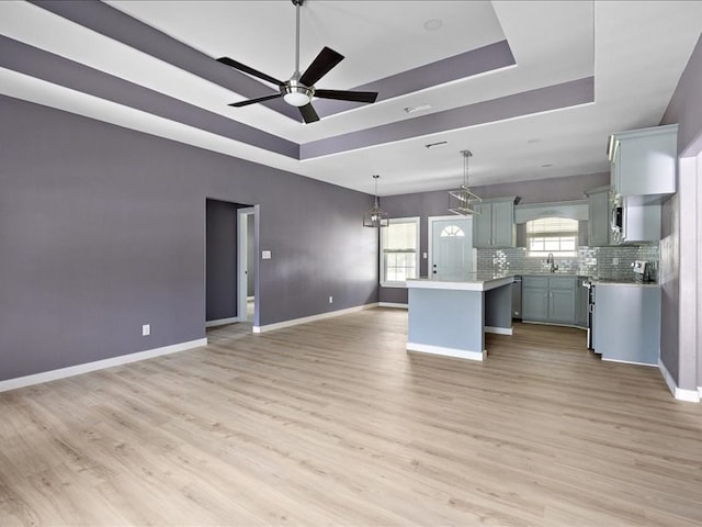 unfurnished living room with a tray ceiling, ceiling fan, and light hardwood / wood-style floors