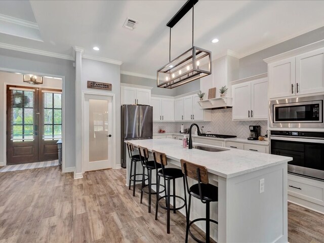 kitchen featuring white cabinets, appliances with stainless steel finishes, light hardwood / wood-style flooring, and an island with sink