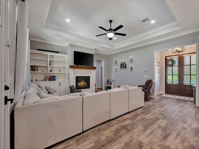 living room featuring a tray ceiling, wood-type flooring, ceiling fan with notable chandelier, and ornamental molding