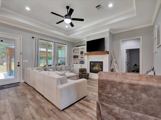 living room with light wood-type flooring, a tray ceiling, and plenty of natural light