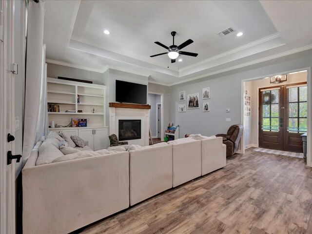 living room with ceiling fan with notable chandelier, a raised ceiling, wood-type flooring, and crown molding