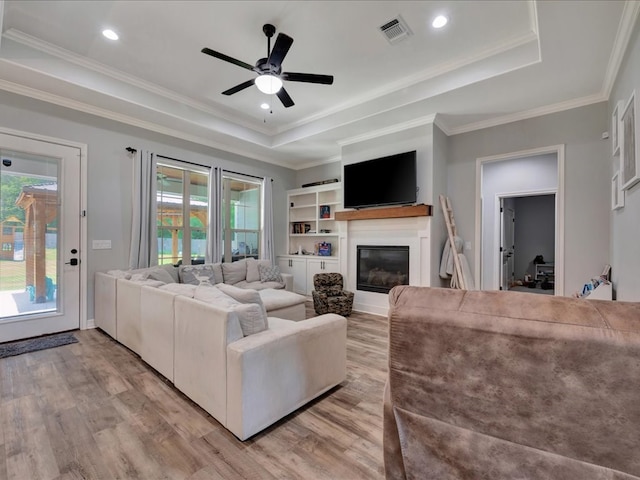 living room with a raised ceiling, crown molding, a healthy amount of sunlight, and light hardwood / wood-style floors