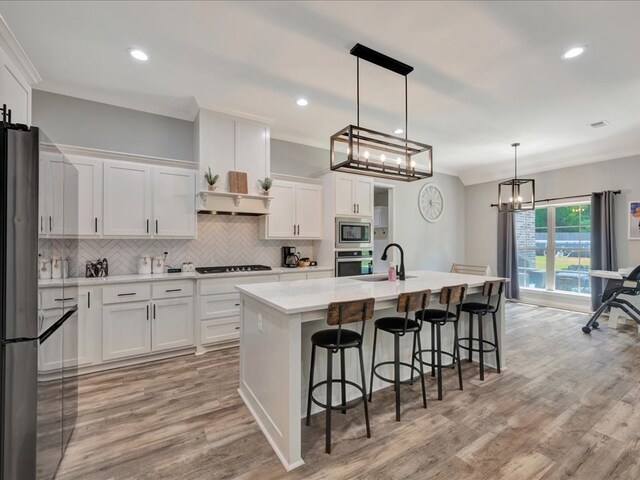 kitchen with white cabinets, light hardwood / wood-style floors, a kitchen island with sink, and hanging light fixtures