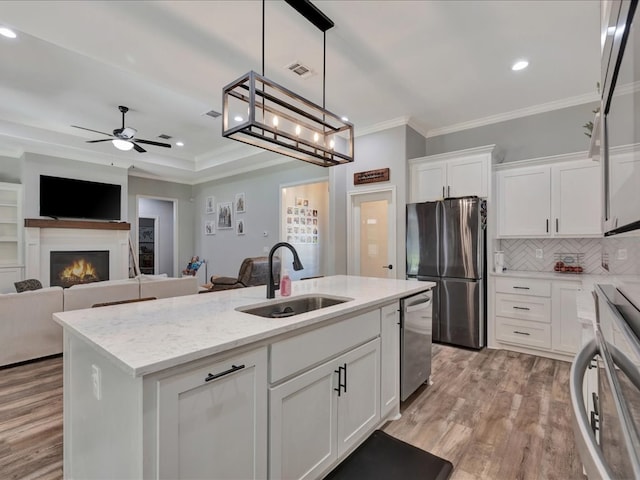 kitchen with sink, appliances with stainless steel finishes, a center island with sink, white cabinets, and light wood-type flooring