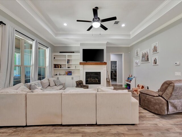 living room featuring a tray ceiling, crown molding, ceiling fan, and light wood-type flooring