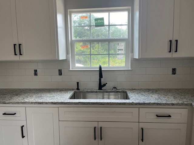 kitchen with decorative backsplash, white cabinets, light stone countertops, and a sink