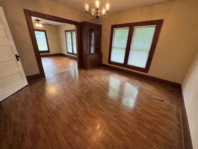 empty room featuring a textured wall, wood finished floors, baseboards, a textured ceiling, and a notable chandelier
