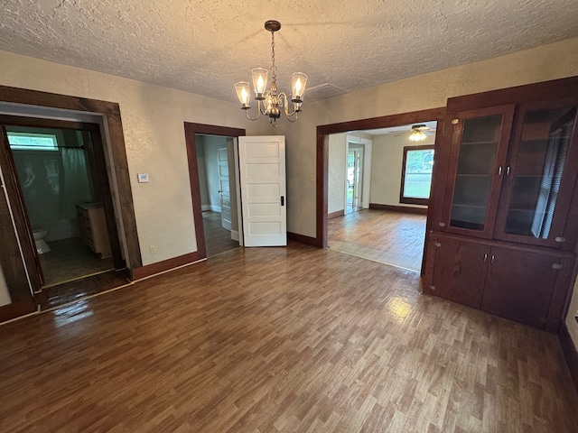 unfurnished dining area featuring baseboards, wood finished floors, a textured ceiling, and ceiling fan with notable chandelier