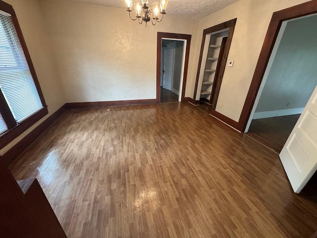 unfurnished dining area with a textured ceiling, baseboards, an inviting chandelier, wood finished floors, and a textured wall