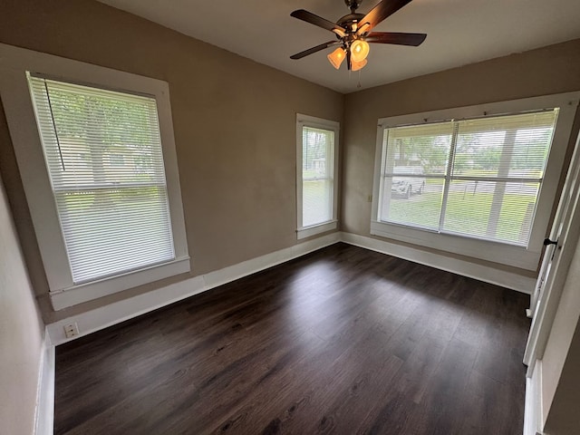 spare room featuring baseboards, dark wood-style floors, a wealth of natural light, and ceiling fan