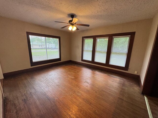 empty room featuring a wealth of natural light, a ceiling fan, wood finished floors, and a textured ceiling