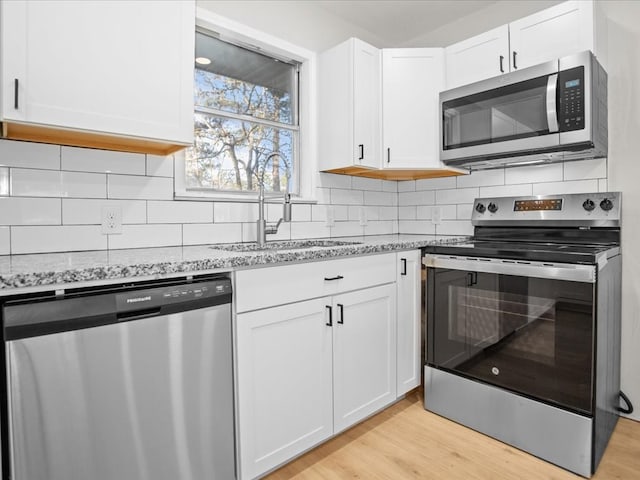 kitchen with sink, light hardwood / wood-style flooring, light stone countertops, appliances with stainless steel finishes, and white cabinetry