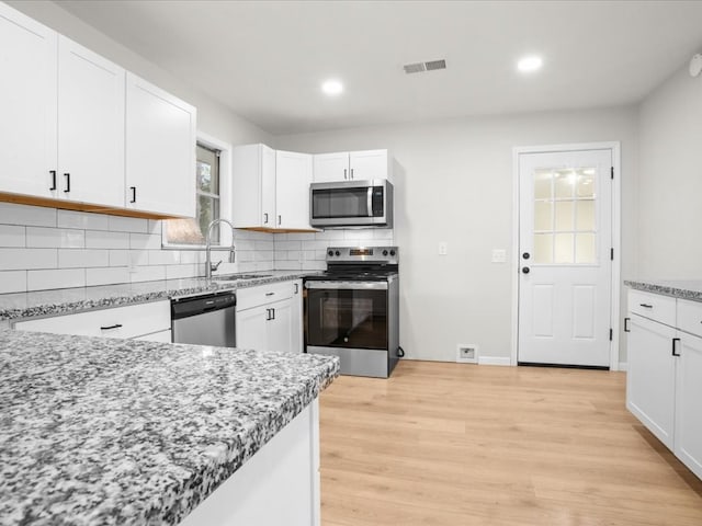 kitchen with light stone countertops, appliances with stainless steel finishes, light hardwood / wood-style floors, and white cabinetry