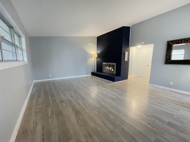 unfurnished living room with a large fireplace, light hardwood / wood-style floors, and vaulted ceiling