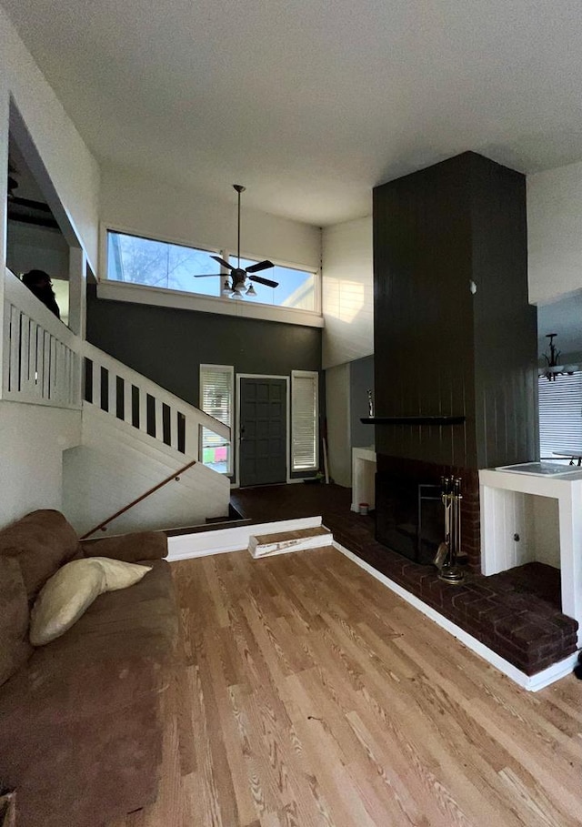 unfurnished living room with a high ceiling, a brick fireplace, ceiling fan, and hardwood / wood-style floors