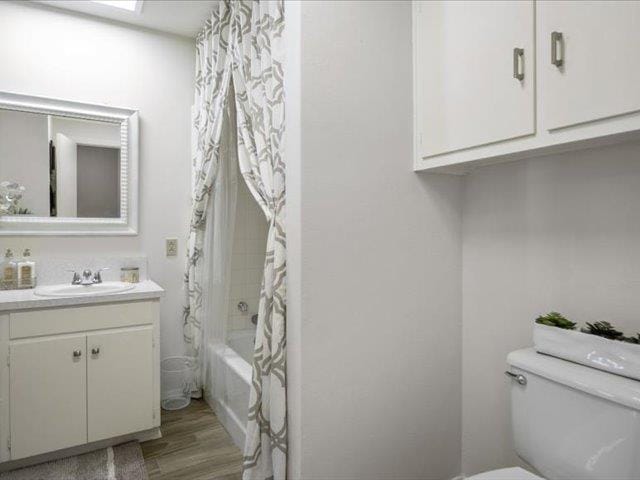 full bathroom featuring hardwood / wood-style floors, vanity, shower / bath combination with curtain, and toilet