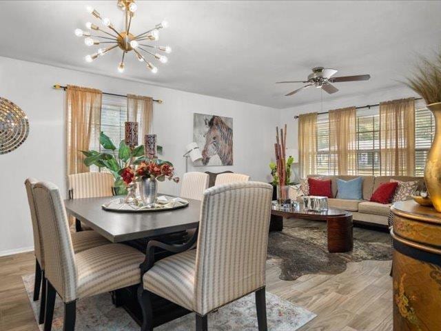 dining space with ceiling fan with notable chandelier and hardwood / wood-style flooring