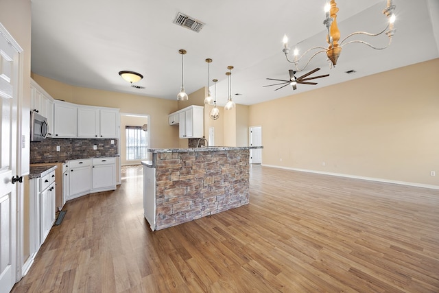 kitchen with backsplash, a kitchen island with sink, pendant lighting, white cabinets, and light hardwood / wood-style floors