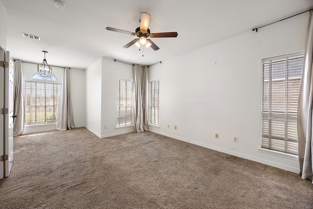 carpeted spare room featuring ceiling fan with notable chandelier