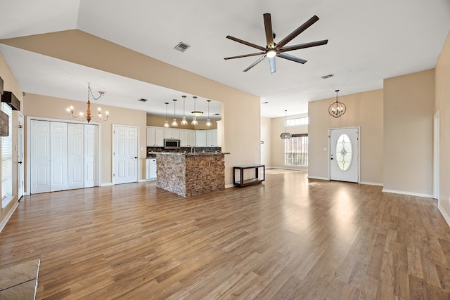 unfurnished living room with vaulted ceiling, light hardwood / wood-style floors, and ceiling fan with notable chandelier