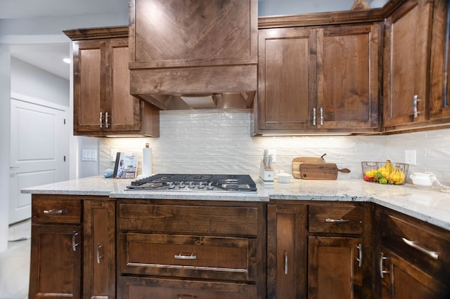 kitchen featuring custom range hood, stainless steel gas cooktop, light stone countertops, and tasteful backsplash