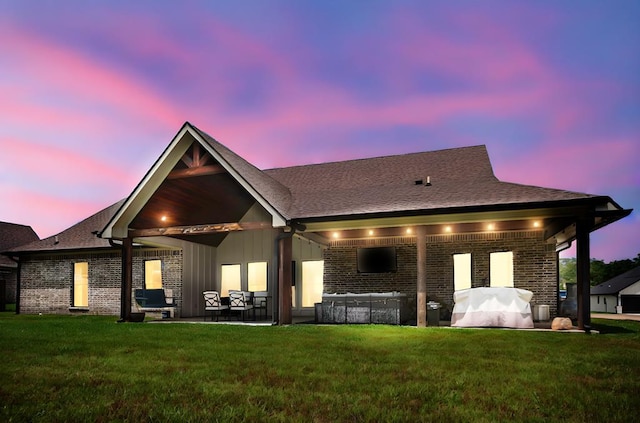 back of property at dusk featuring a lawn, brick siding, and a patio area