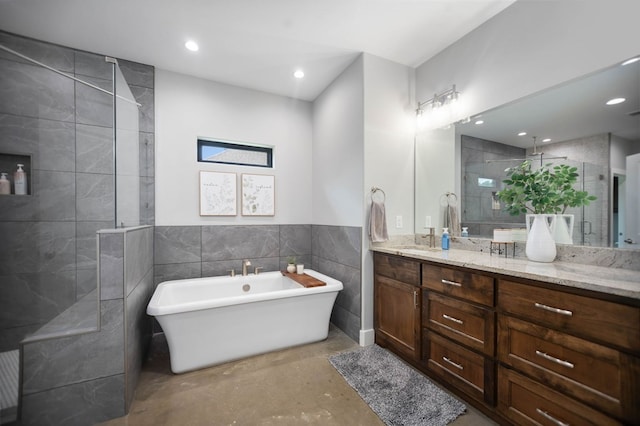 full bath featuring vanity, a freestanding tub, tile walls, tiled shower, and recessed lighting