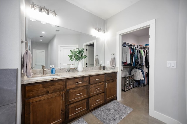 bathroom with double vanity, concrete flooring, baseboards, and a walk in closet