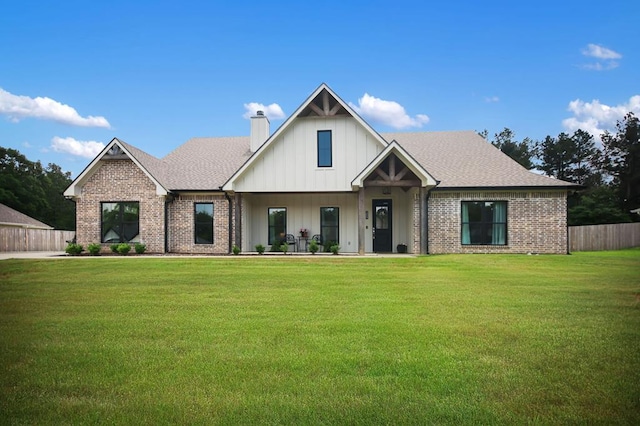 view of front facade with board and batten siding, a chimney, brick siding, fence, and a front lawn